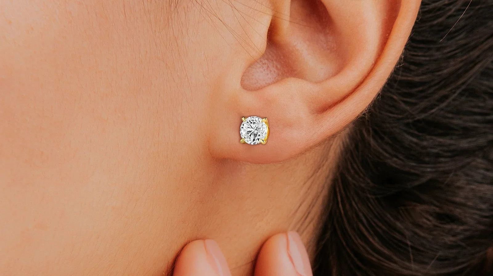 Close-up of a person wearing a pair of sparkling diamond stud earrings in a yellow gold setting