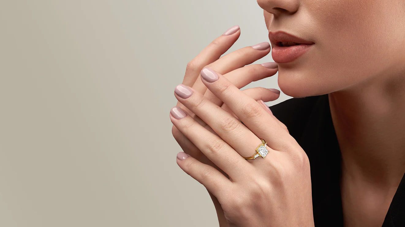 Close-up of a woman's hand wearing a gold ring with a large, radiant-cut diamond and two smaller baguette diamonds