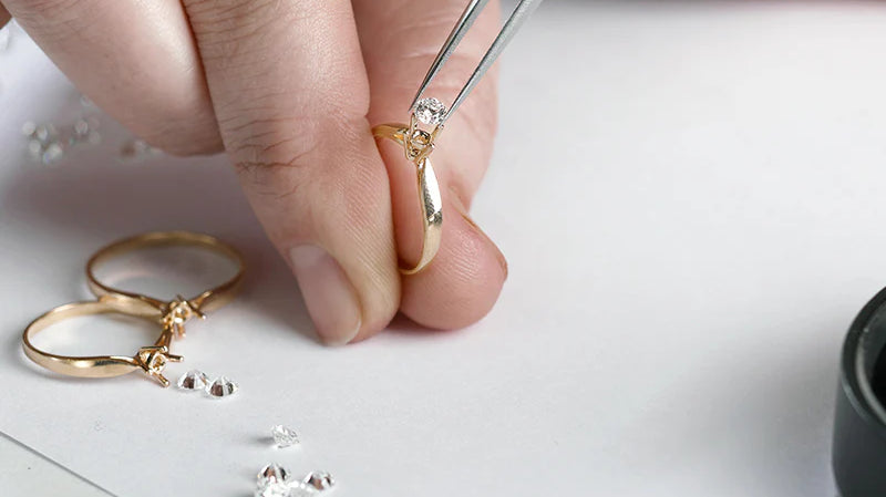 Jeweler setting a diamond in a gold ring using tweezers. Small diamonds are scattered on the workbench