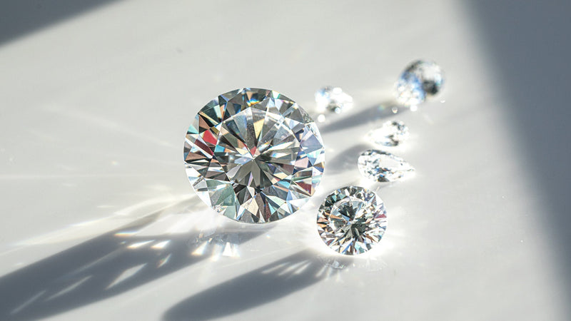 Close-up photograph of brilliant-cut diamonds on a white surface with dramatic lighting, showing their sparkle, fire, and clarity