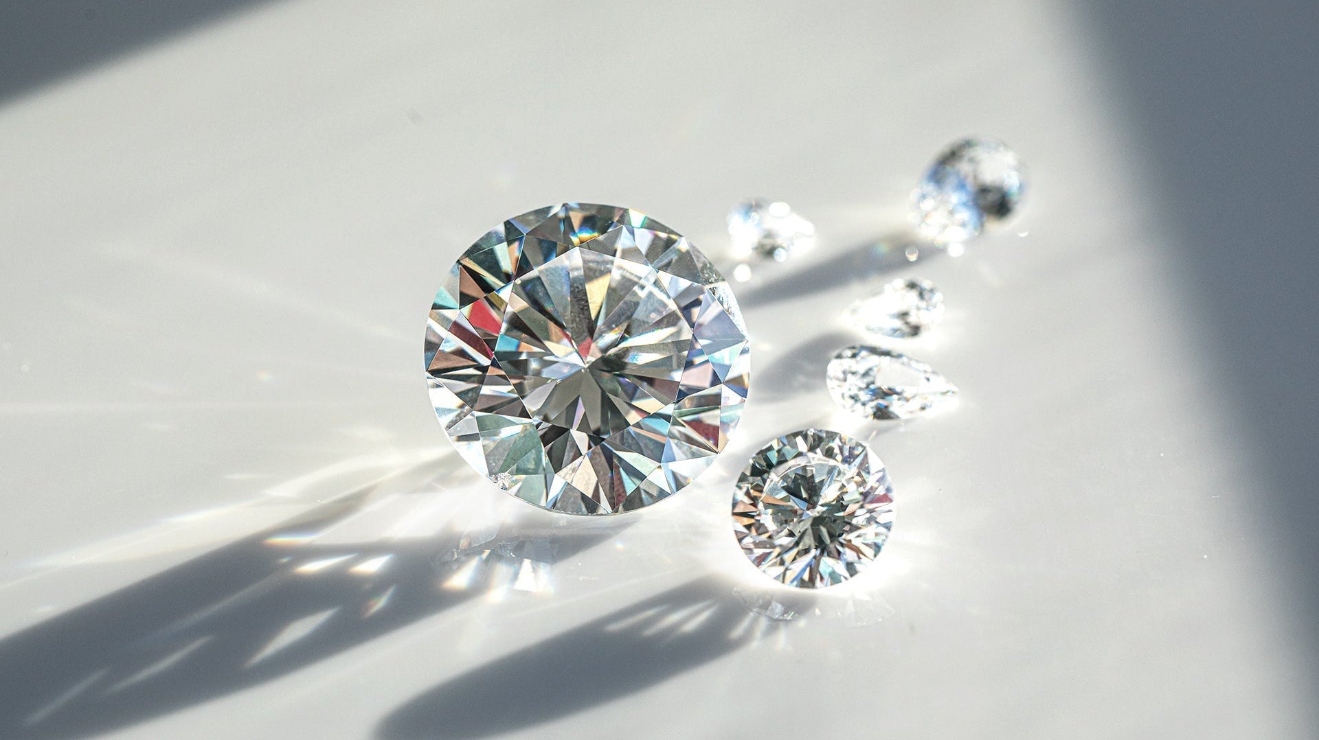 Close-up photograph of brilliant-cut diamonds on a white surface with dramatic lighting, showing their sparkle, fire, and clarity