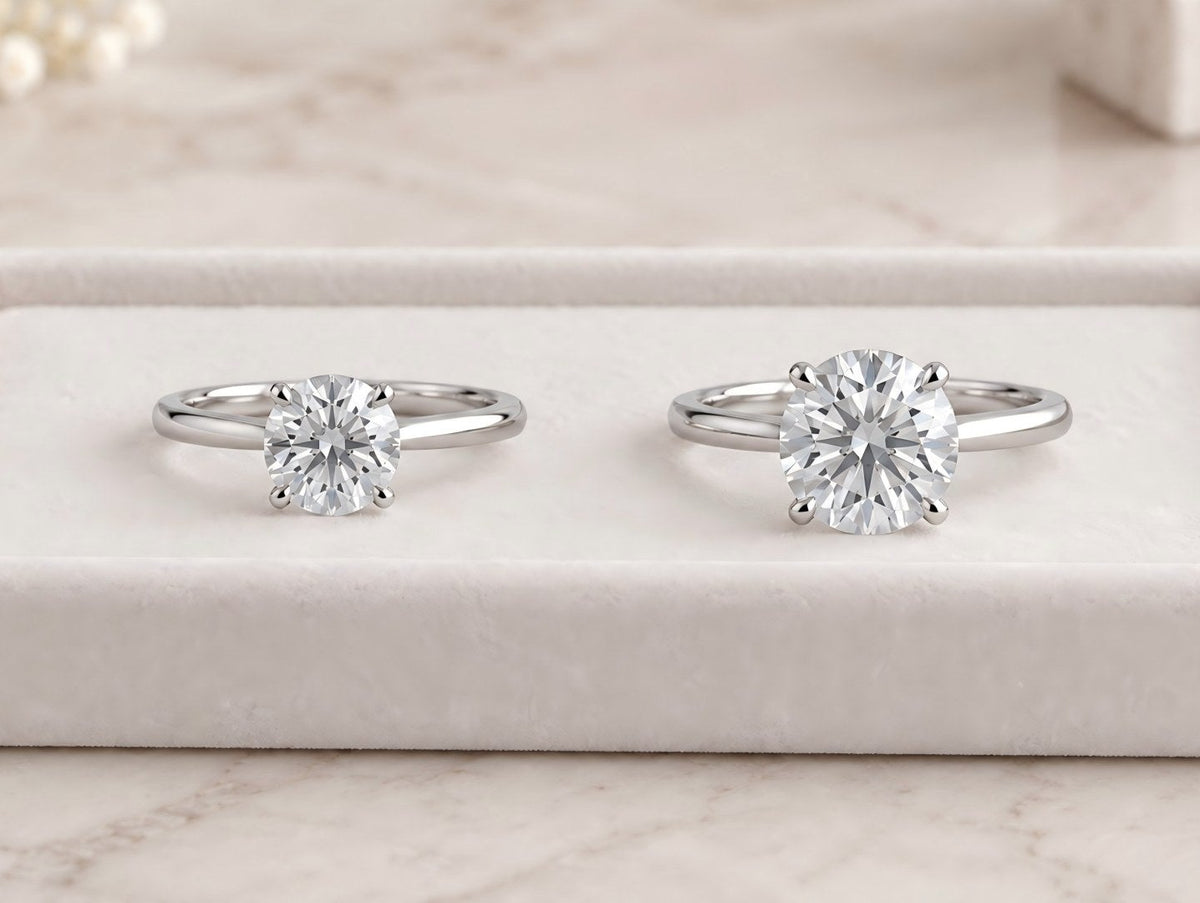 Two round solitaire diamond rings displayed side by side in a white jewelry display tray.