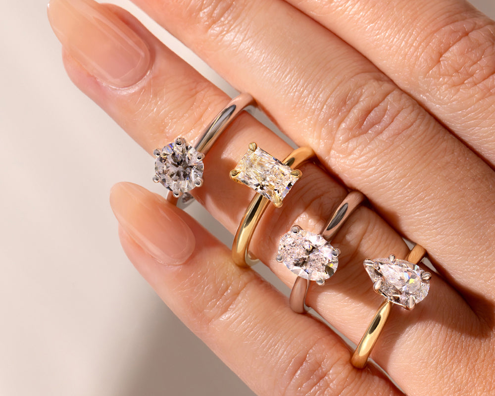 Hand wearing multiple lab diamond engagement rings on a neutral background