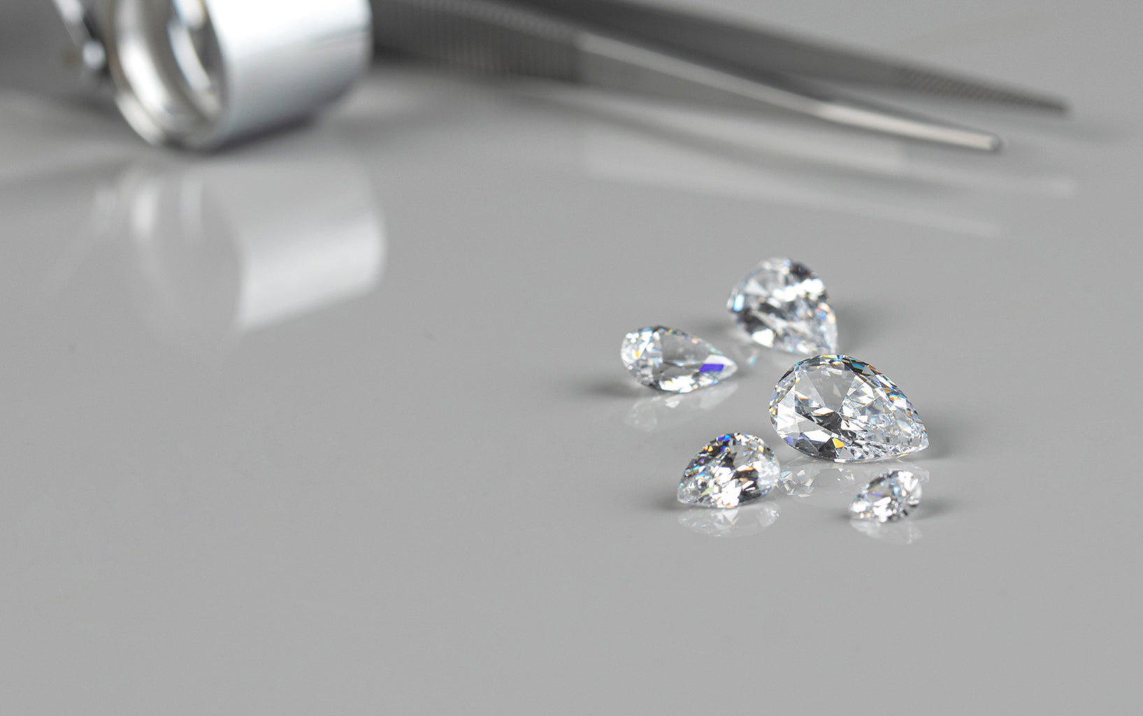 Lab diamonds on a gray surface with tweezers.