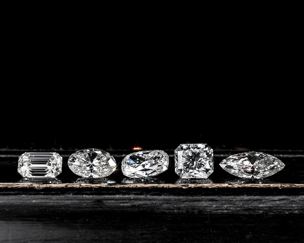 Five lab diamonds of different shapes and sizes on a dark background