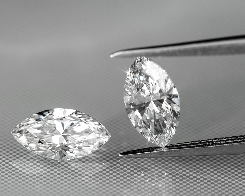 Two marquise-shaped lab diamonds held by tweezers on a gray background
