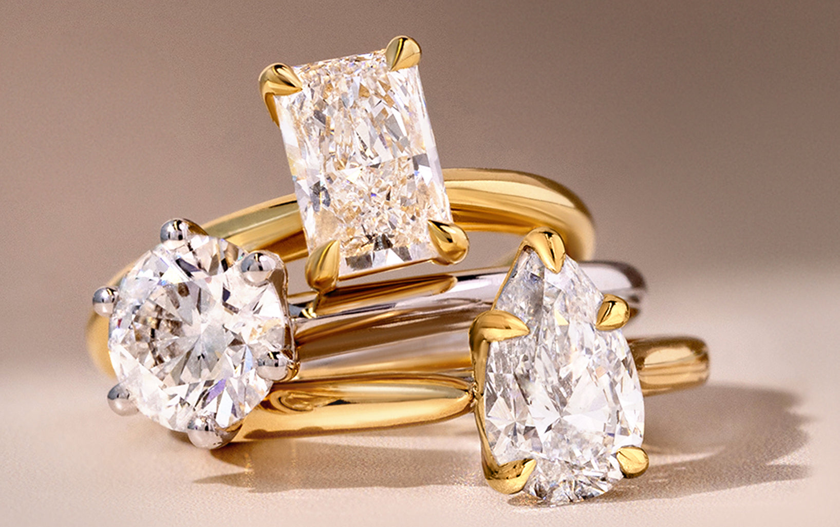 Three Solitaire lab grown diamond engagement rings with gold bands on a light background