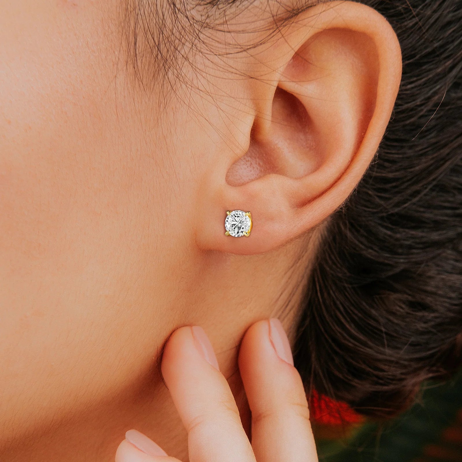 Close-up of a person wearing a pair of sparkling diamond stud earrings in a yellow gold setting