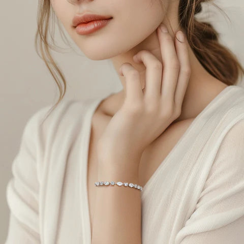 A woman's wrist adorned with a delicate silver bracelet featuring alternating marquise and round diamonds, each secured by a prong setting