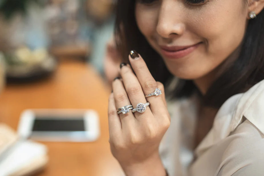 Woman trying on different diamond rings at a jewelry store, comparing styles and sizes