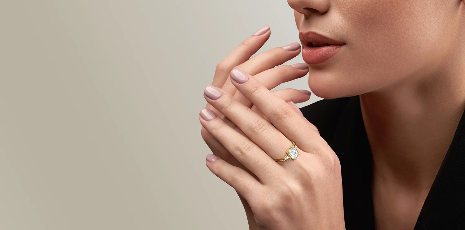 Close-up of a woman's hand wearing a gold ring with a large, radiant-cut diamond and two smaller baguette diamonds