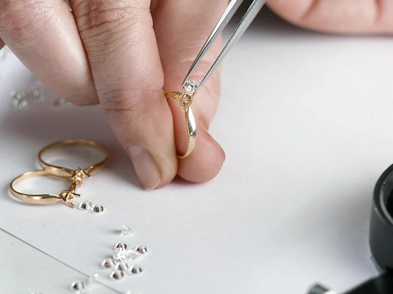 Jeweler setting a diamond in a gold ring using tweezers. Small diamonds are scattered on the workbench