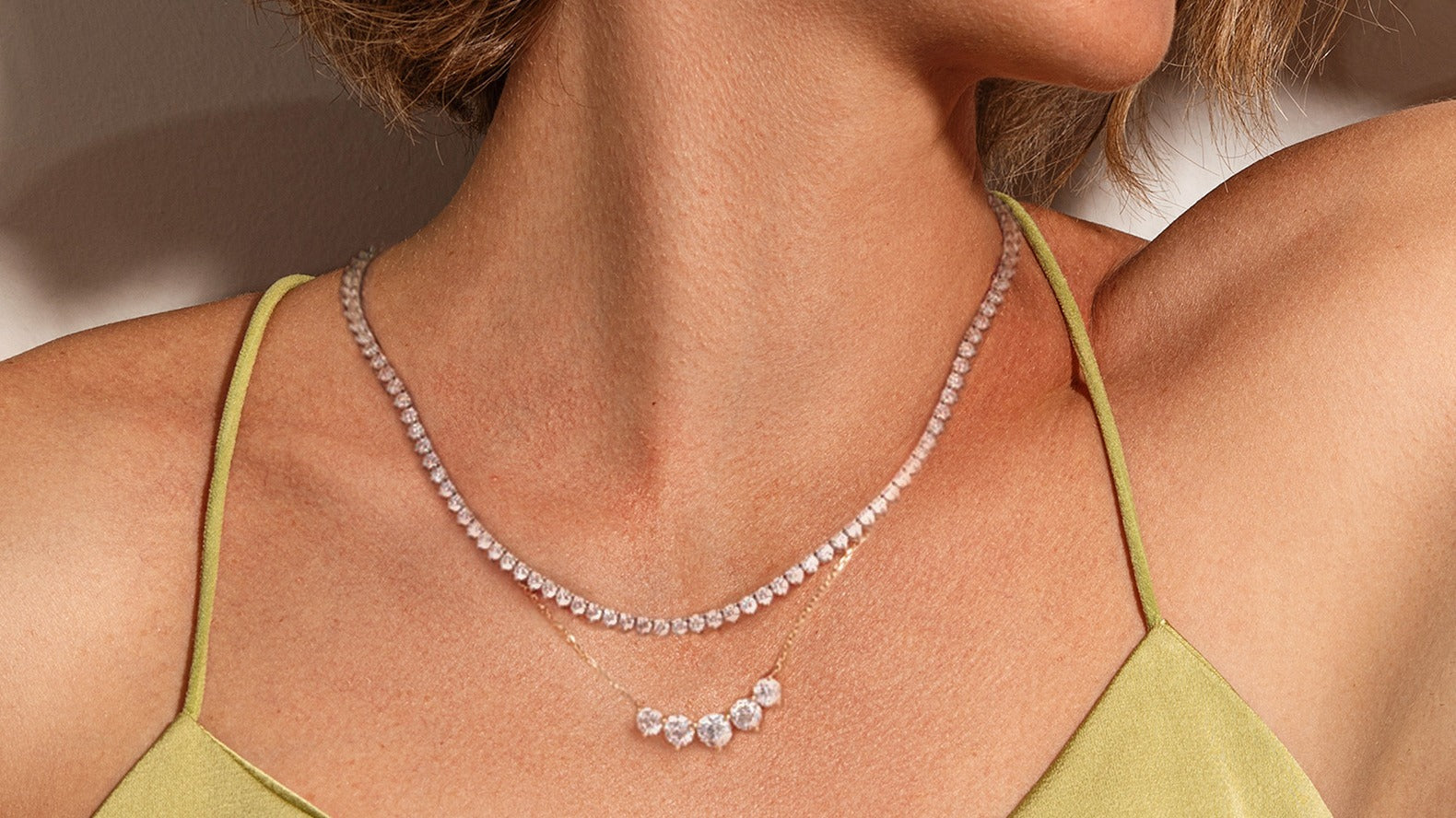 A woman wearing a delicate lab diamond tennis necklace layered with a three-stone diamond pendant necklace