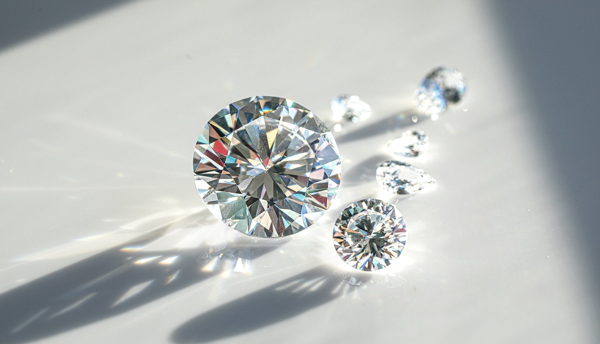 Close-up photograph of brilliant-cut diamonds on a white surface with dramatic lighting, showing their sparkle, fire, and clarity