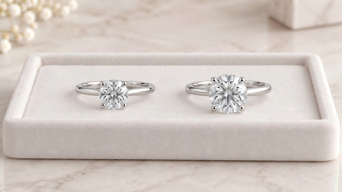 Two round solitaire diamond rings displayed side by side in a white jewelry display tray.