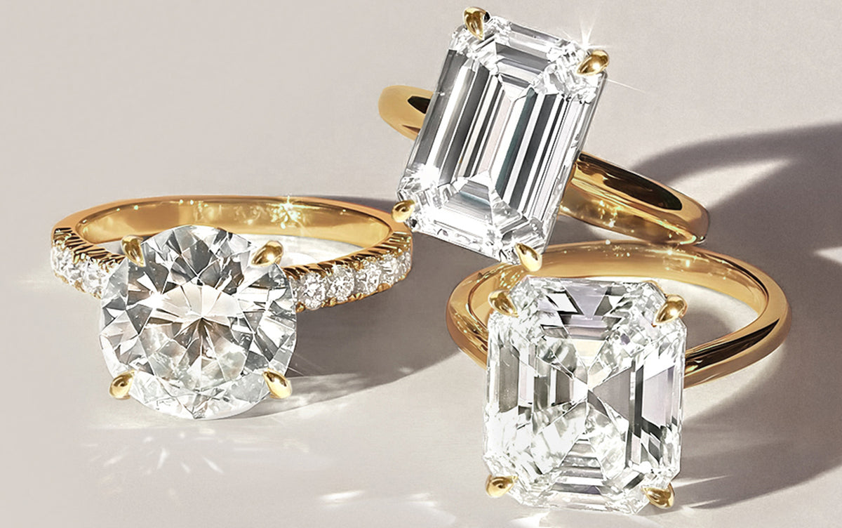 Three lab grown diamond engagement rings with gold bands on a light background