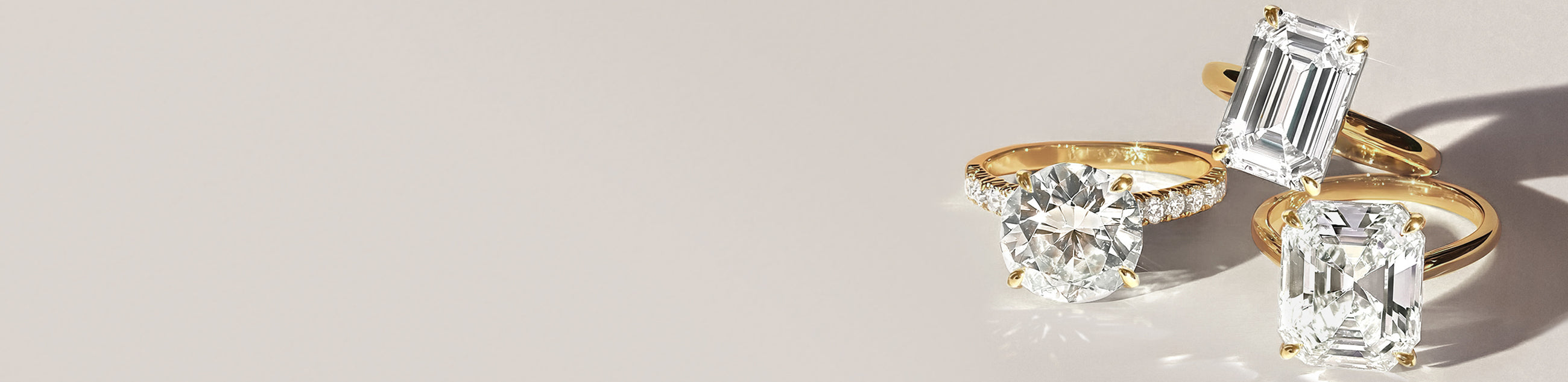 Three lab grown diamond engagement rings with gold bands on a light background