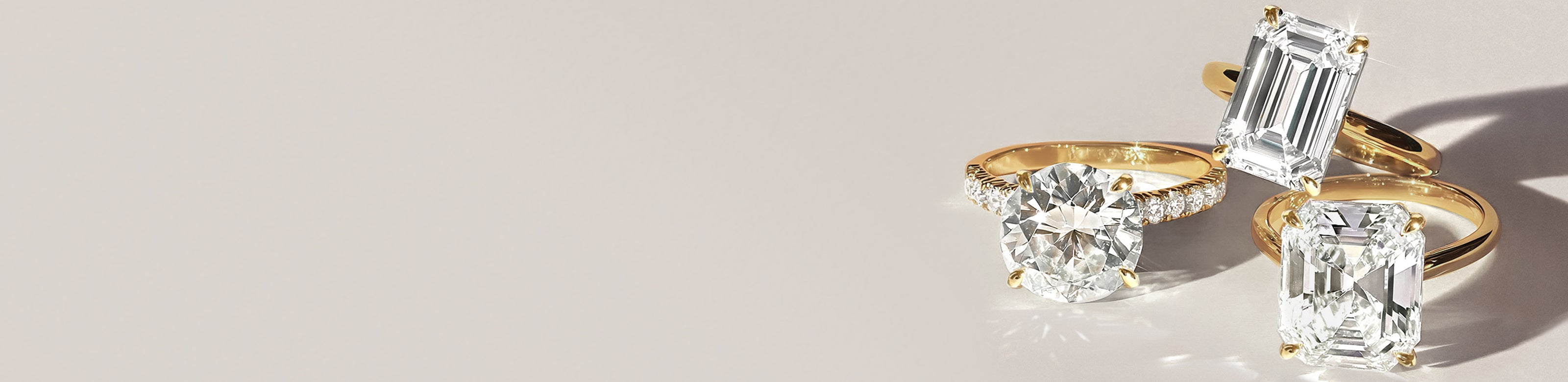 Three lab grown diamond engagement rings with gold bands on a light background