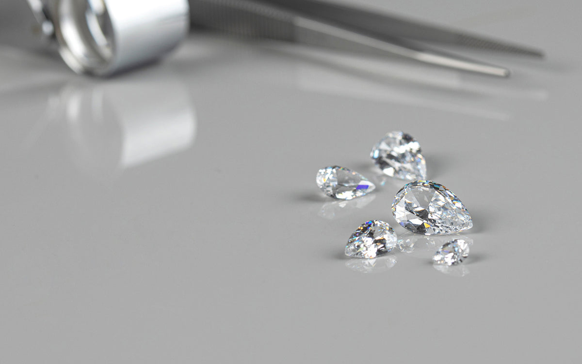 Lab diamonds on a gray surface with tweezers.
