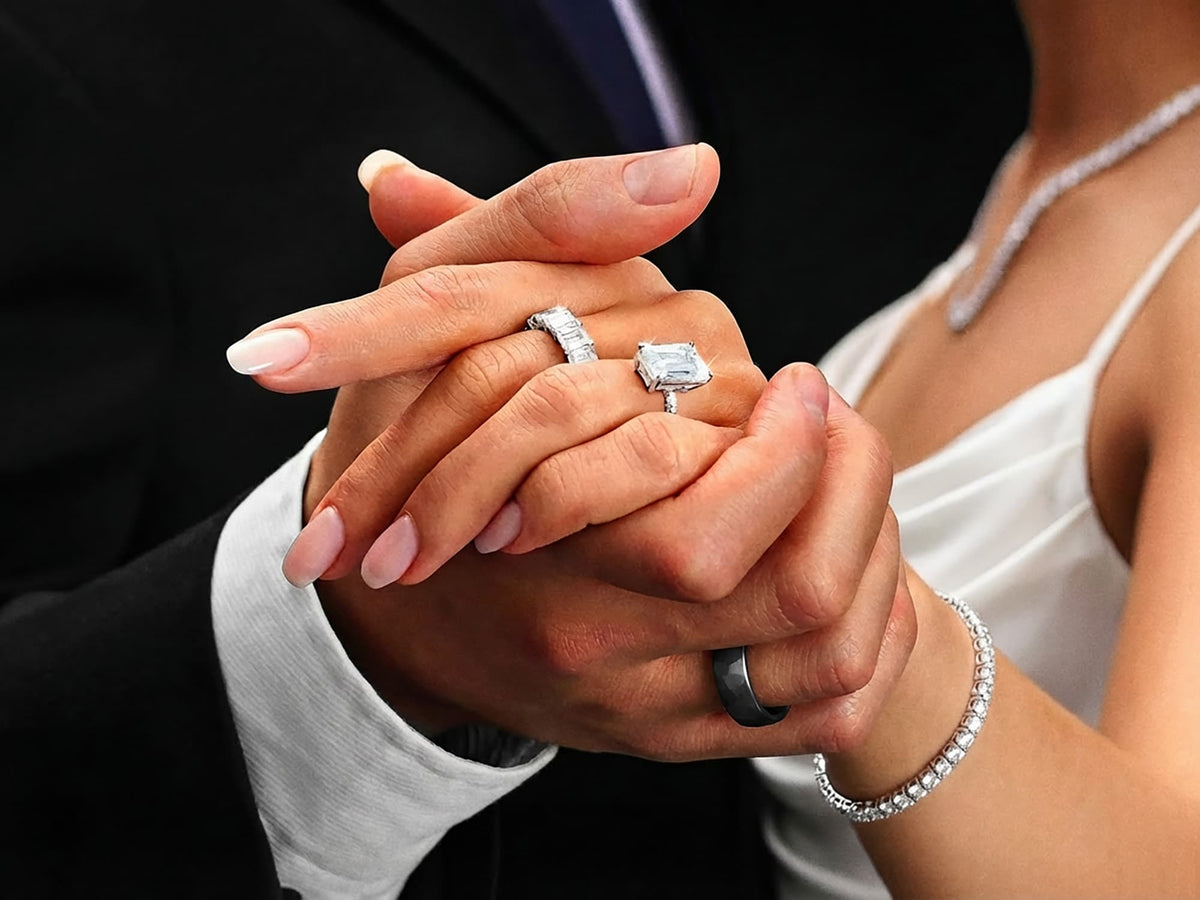 Close-up of hands holding each other with diamond engagement rings on a black background