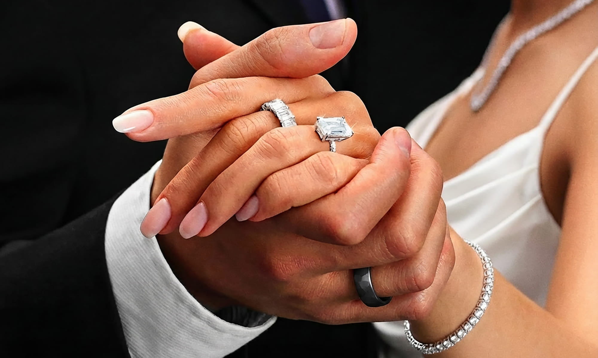 Close-up of hands holding each other with diamond engagement rings on a black background