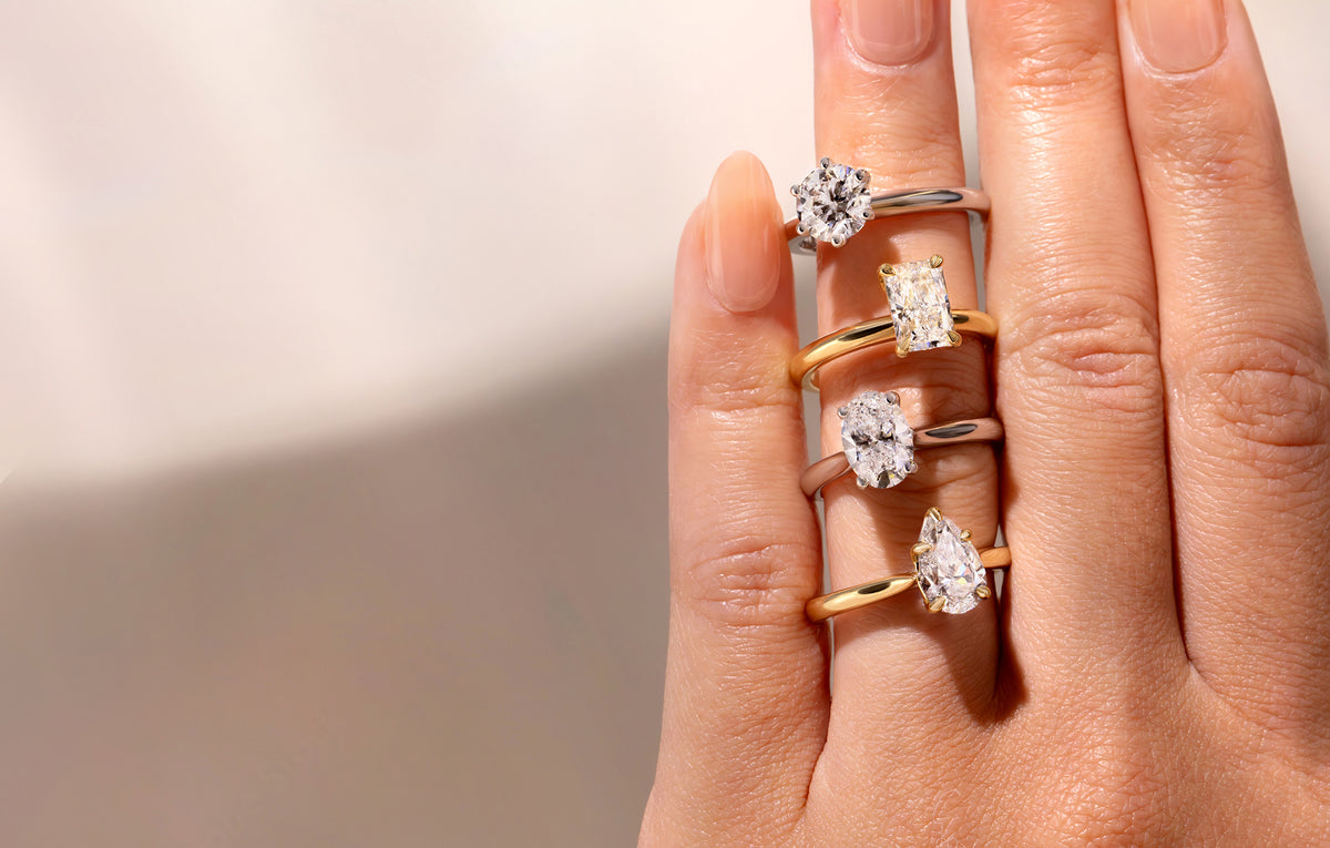 Hand wearing multiple lab grown diamond engagement rings on a light background