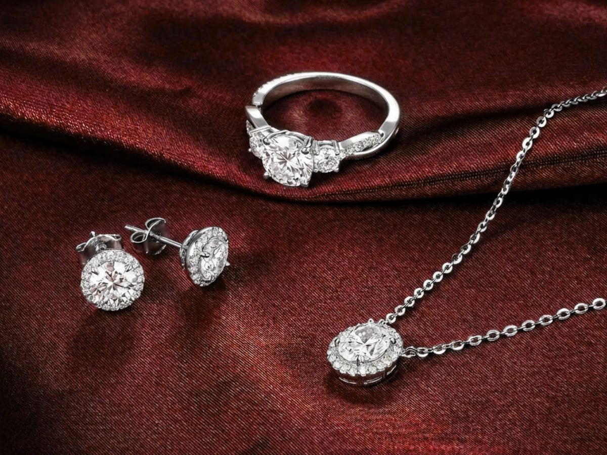 White gold jewelry set including a diamond ring, necklace, and earrings on a red fabric background