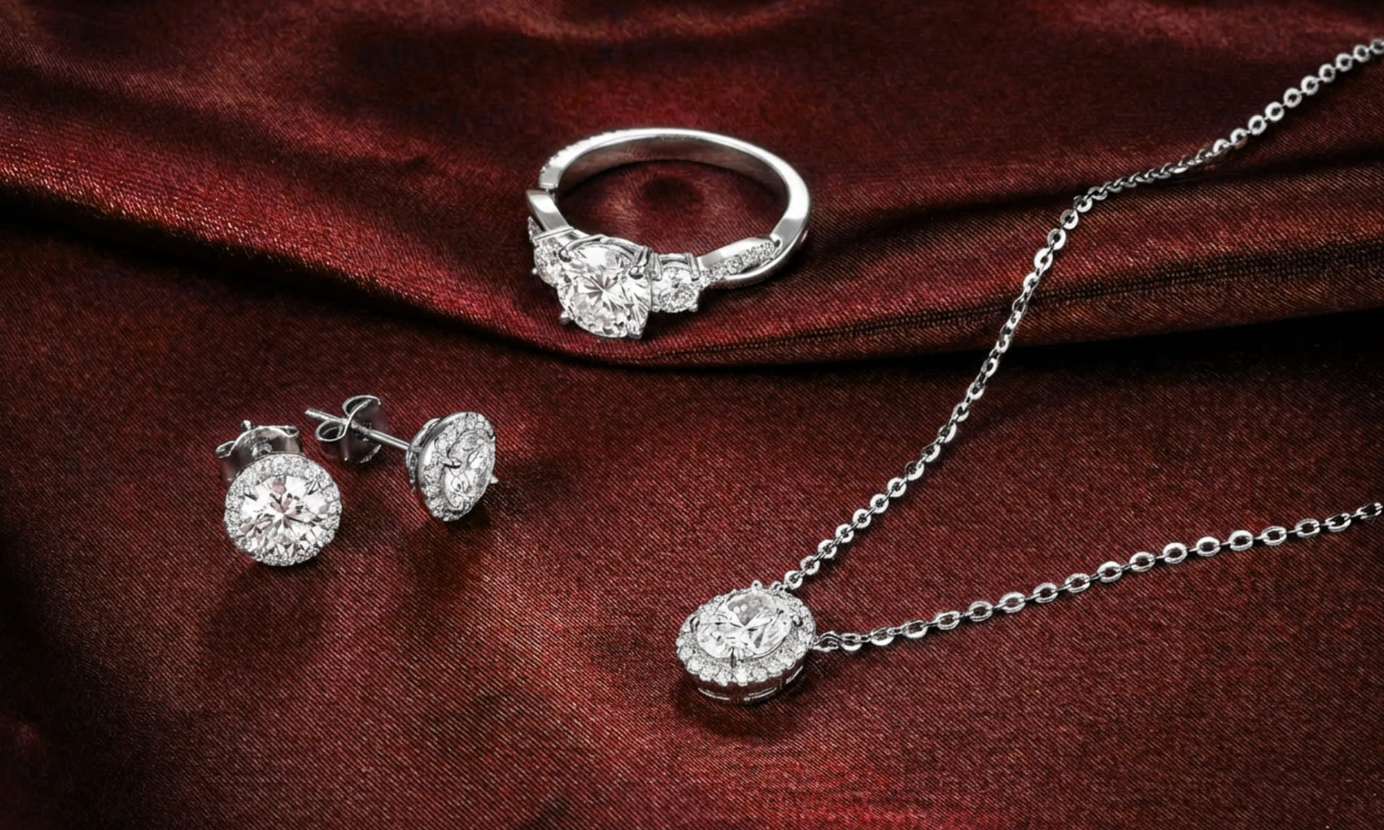 White gold jewelry set including a diamond ring, necklace, and earrings on a red fabric background