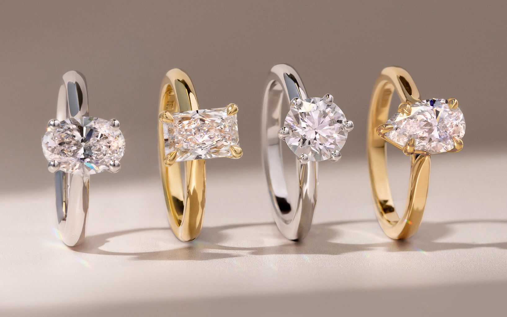 Four lab diamond engagement rings in different metal on a neutral background