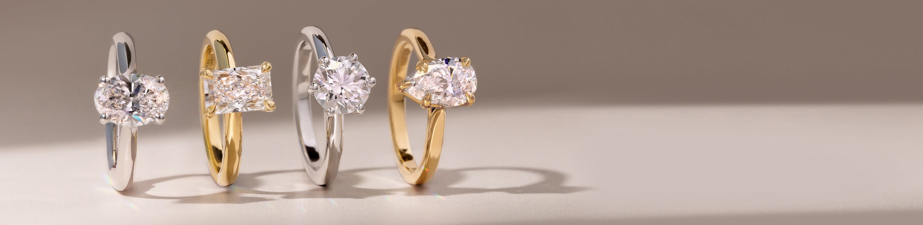 Four lab diamond engagement rings in different metal on a neutral background