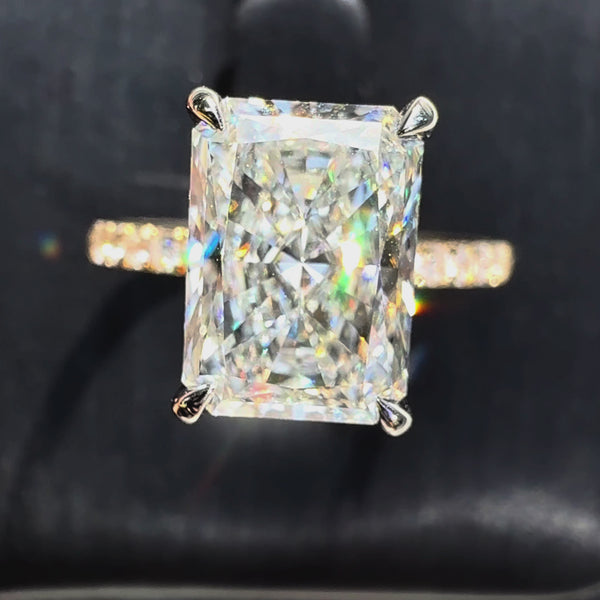 Radiant-cut diamond engagement ring featuring a four-prong setting and a sparkling pavé yellow gold band, shown against a dark textured background.