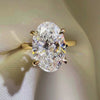 A large 3ct oval-cut lab diamond engagement ring set in a four-prong yellow gold band, resting on a cream-colored satin jewelry box liner.