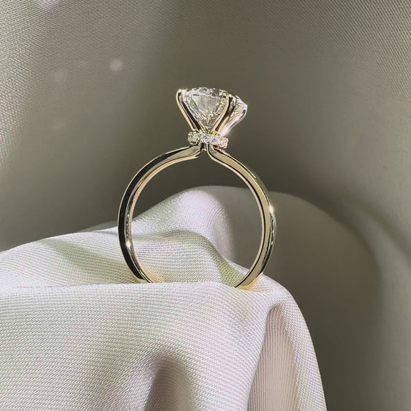 Side view of a round-cut diamond engagement ring featuring a hidden halo and a cathedral-style yellow gold band.