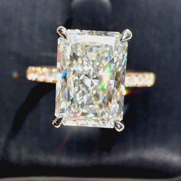 Radiant-cut diamond engagement ring featuring a four-prong setting and a sparkling pavé yellow gold band, shown against a dark textured background.