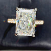 Radiant-cut diamond engagement ring featuring a four-prong setting and a sparkling pavé yellow gold band, shown against a dark textured background.