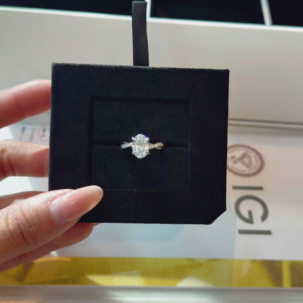 Oval-cut lab diamond engagement ring with a pavé-set twisted infinity band, displayed in a black velvet jewelry insert with an IGI certification report in the background.