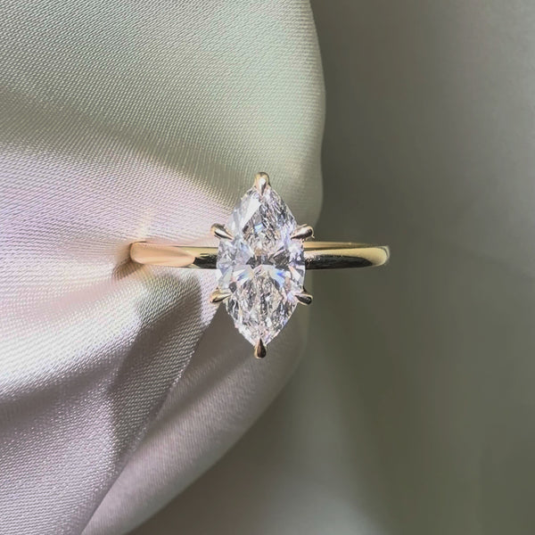 Marquise-cut lab diamond engagement ring featuring a six-prong setting on a polished yellow gold band, displayed against a white satin background.