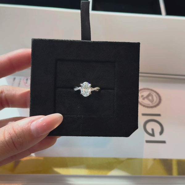 Oval-cut lab diamond engagement ring with a pavé-set twisted infinity band, displayed in a black velvet jewelry insert with an IGI certification report in the background.