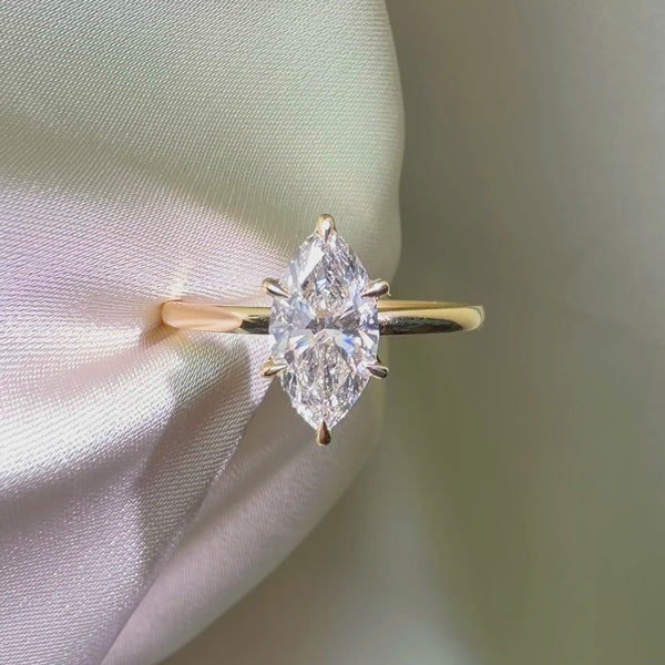 Marquise-cut lab diamond engagement ring featuring a six-prong setting on a polished yellow gold band, displayed against a white satin background.