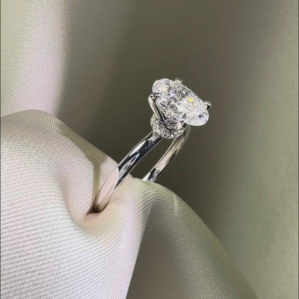 Side profile of an oval-cut diamond engagement ring featuring a hidden halo and a diamond-encrusted basket on a polished white gold band.